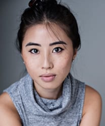 Emma Lau smiling, wearing a navy blazer, with shoulder-length dark hair and a neutral background.