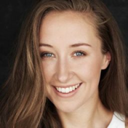 Erin Doherty smiling, wearing a black dress, with long brown hair and minimal makeup.