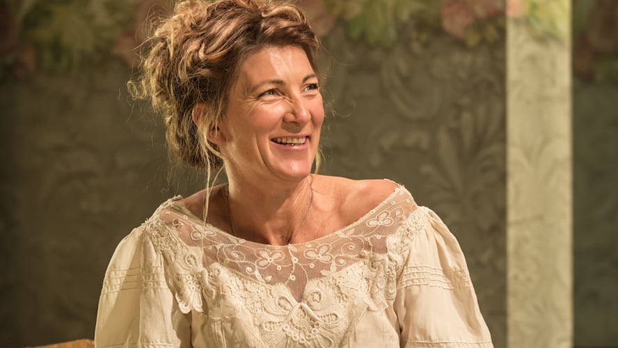 Eve Best as Mrs Arbuthnot, wearing a period costume, seated on a stage set.
