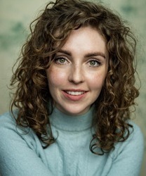 Eve Norris smiling, wearing a blue blouse, with long brown hair and a neutral background.