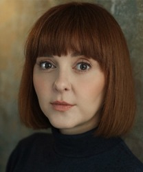 Evelyn Hoskins smiling, wearing a blue blouse, with shoulder-length brown hair and a neutral background.