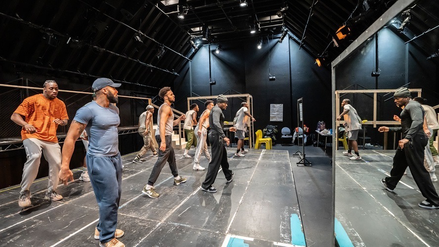 A group of performers rehearsing on stage, with scripts and props scattered around.