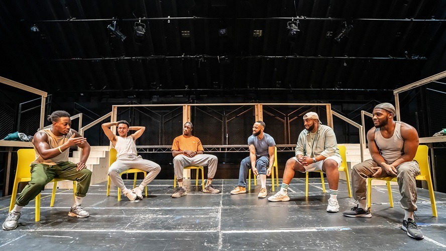 A group of performers rehearsing on stage, with bright lights and a backdrop.