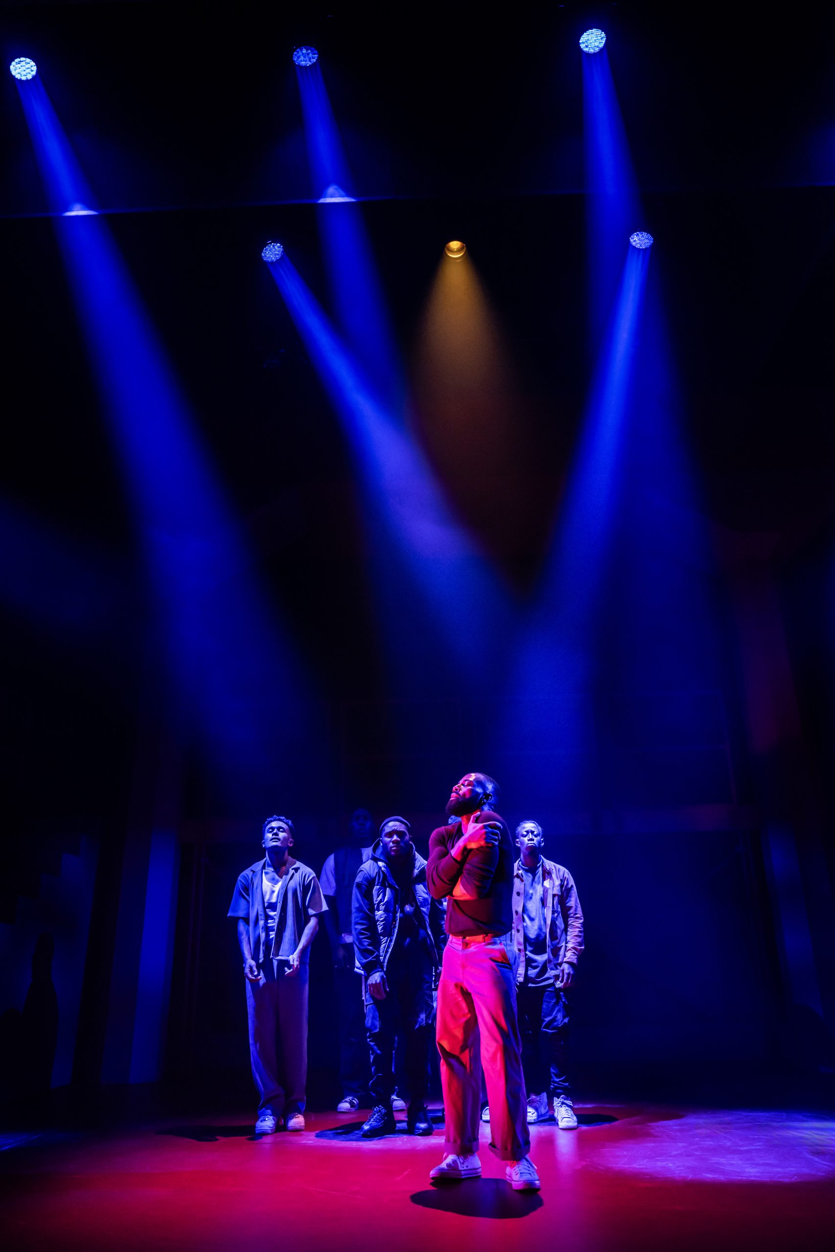 A theatrical performance scene featuring actors on stage with dramatic lighting at the Apollo Theatre, London.