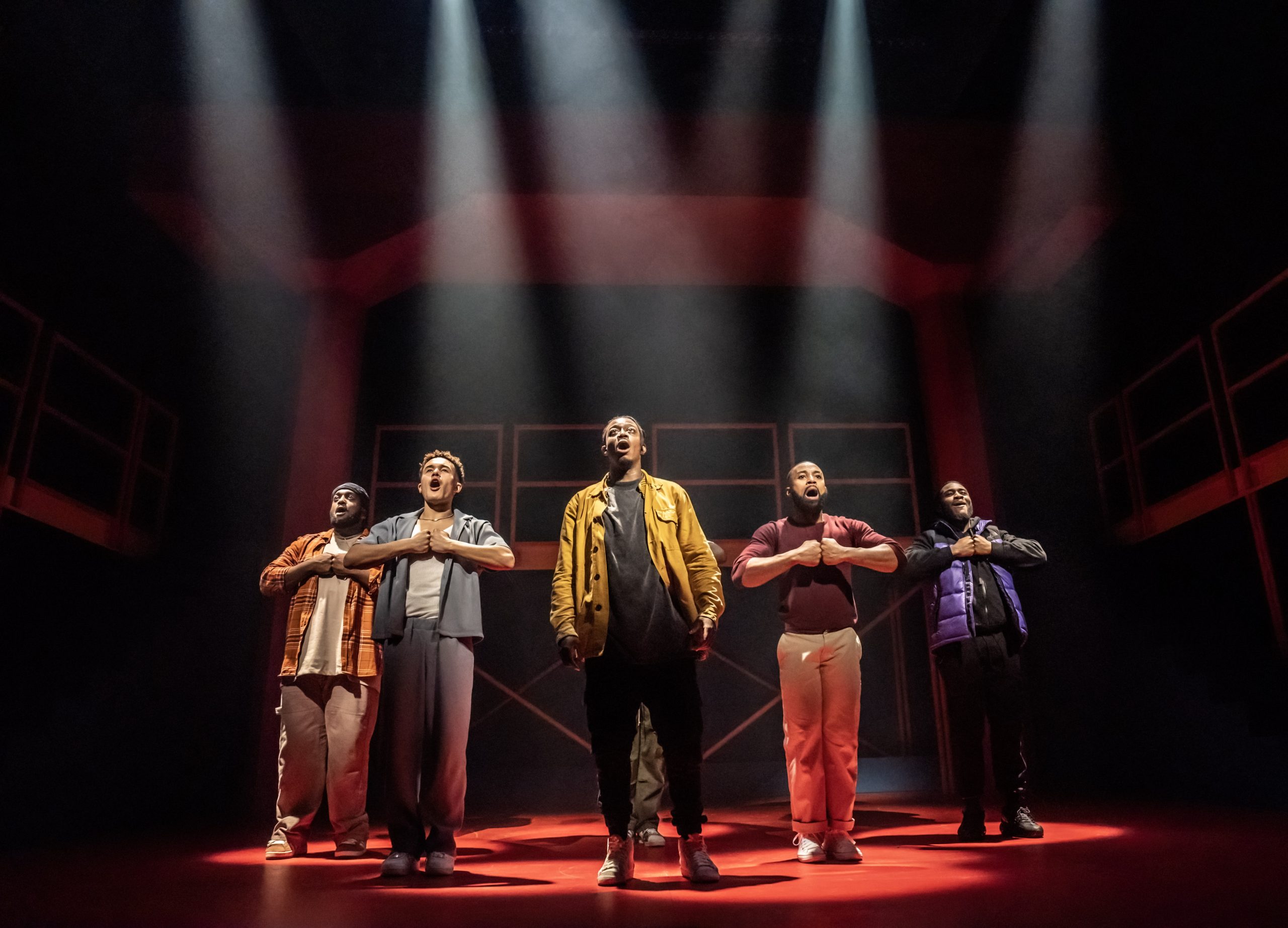 A dramatic stage scene featuring actors in expressive poses, illuminated by focused lighting at Apollo Theatre.