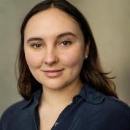 Gabriella Leon smiling, with long brown hair, wearing a black top against a neutral background.
