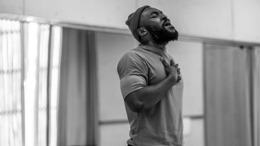 Arinze stands confidently, wearing a casual outfit, with a vibrant backdrop of greenery.