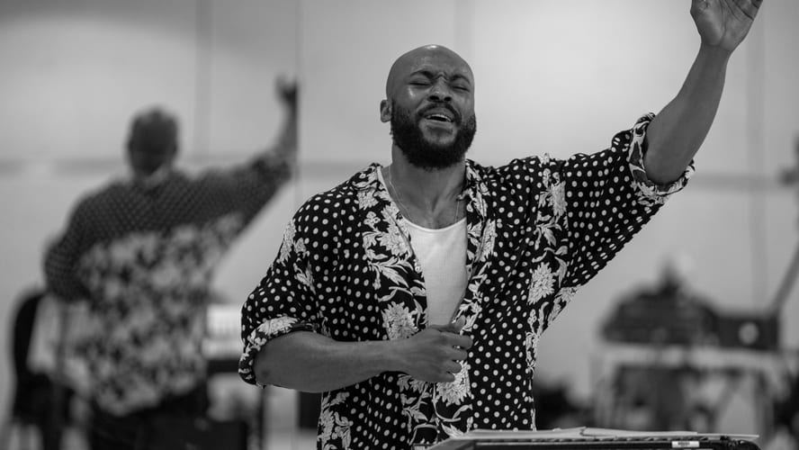 Arinze stands confidently on stage, microphone in hand, with vibrant lighting and an engaged audience.