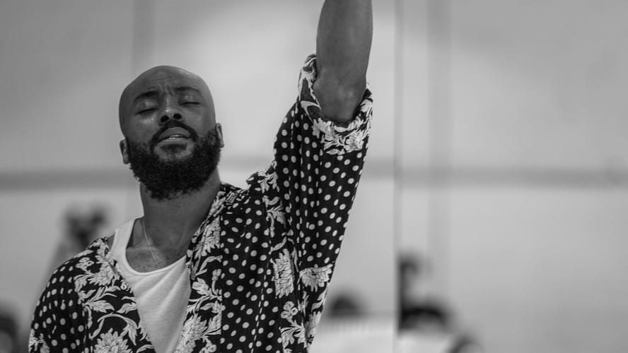 Arinze stands confidently on stage, microphone in hand, with vibrant lighting in the background.