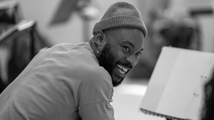 Arinze stands confidently, wearing a casual outfit, against a vibrant urban backdrop.