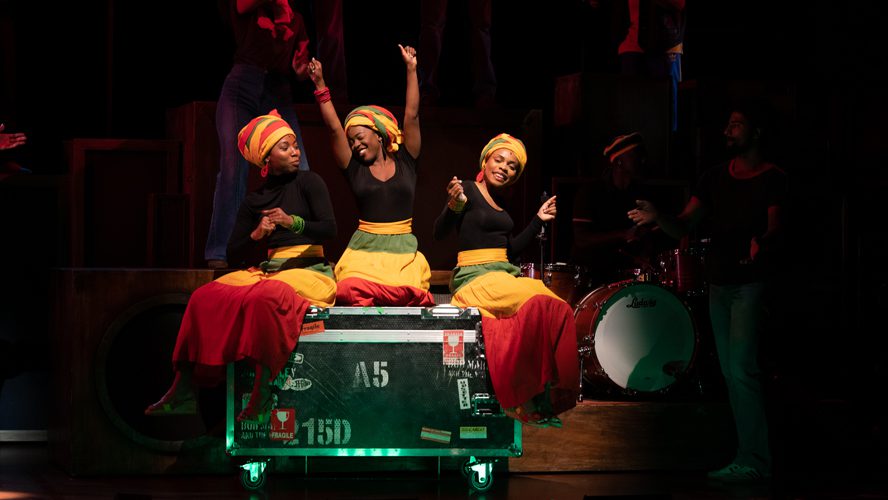 A vibrant stage scene from "Get Up, Stand Up!" featuring performers in dynamic poses and colourful costumes.