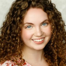 Gracie McGonigal smiling, with long brown hair and wearing a blue blouse against a neutral background.