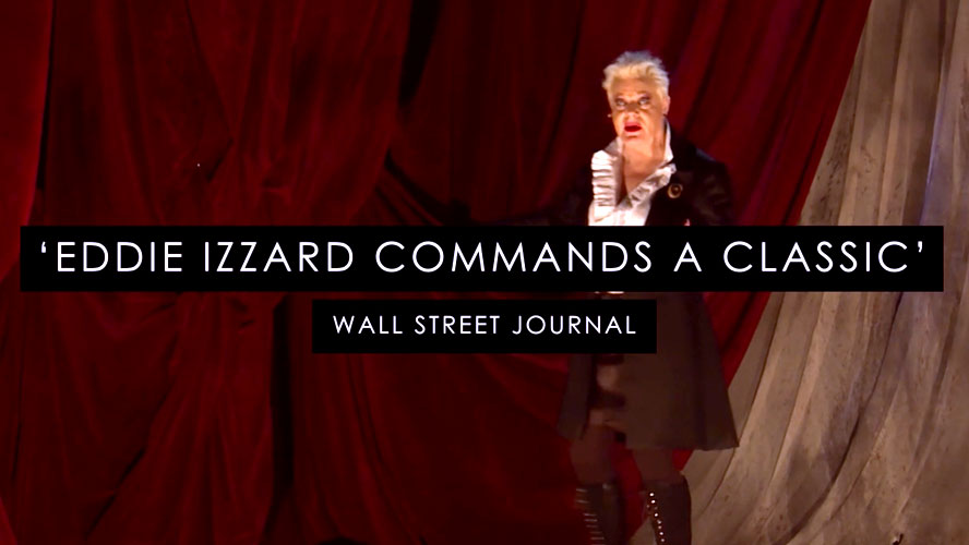 Eddie Izzard as Pip, dressed in period costume, stands in a dramatic, dimly lit setting.