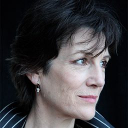 Harriet Walter smiling, wearing a black top, with a blurred background.