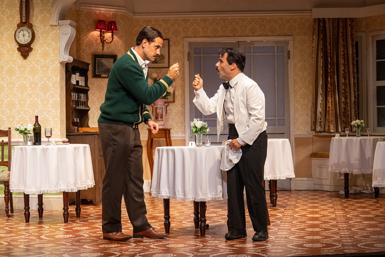 John Cleese as Basil Fawlty, in a hotel setting, interacting with a guest.