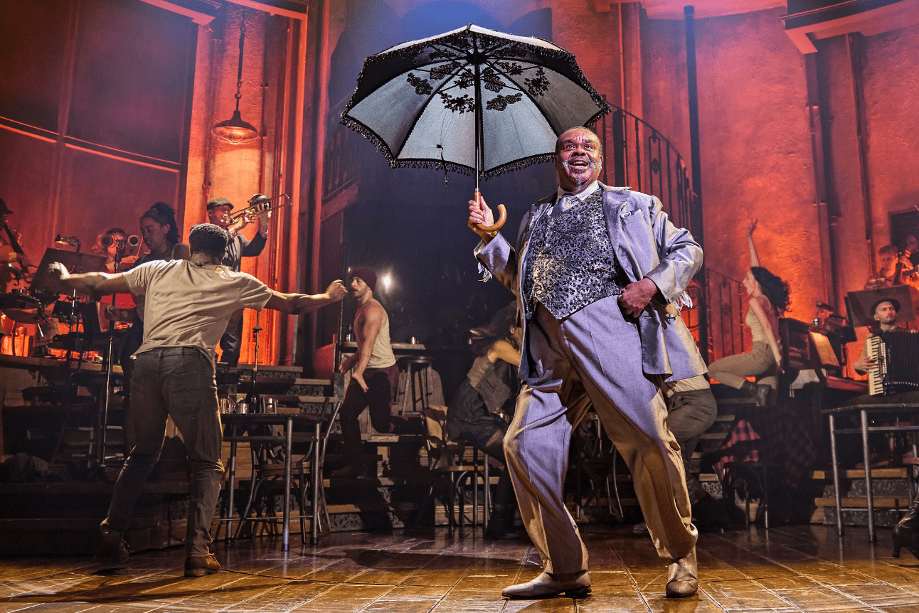 Hermes dances and sings on stage while holding up a fabulous black umbrella