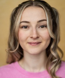 Hannah Lowther smiling, wearing a navy blazer and white blouse, with long brown hair.