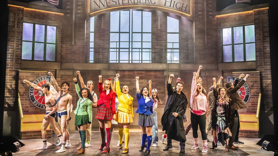 Cast members of Heathers: The Musical performing on stage, dressed in vibrant costumes and expressive poses.