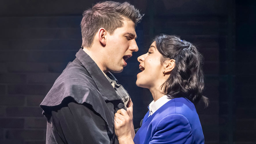 Cast of Heathers: The Musical performing on stage, dressed in vibrant costumes with dramatic lighting.
