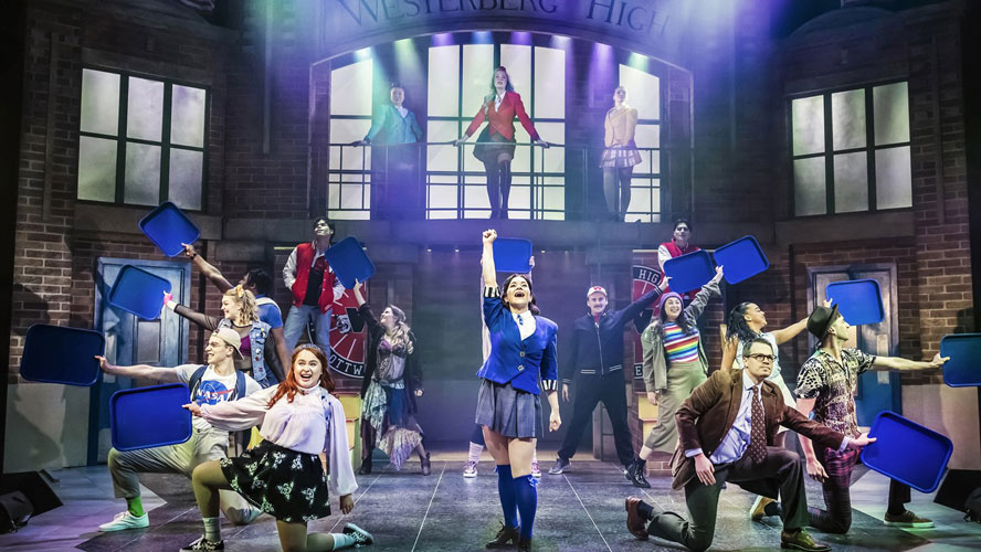 Cast members of Heathers: The Musical performing on stage, dressed in vibrant costumes with expressive poses.