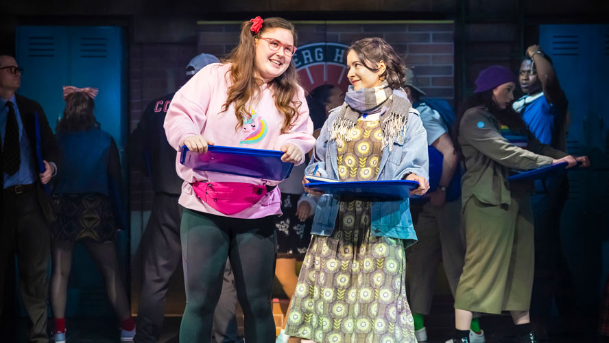 Cast members of Heathers: The Musical performing on stage, dressed in vibrant costumes and expressive poses.