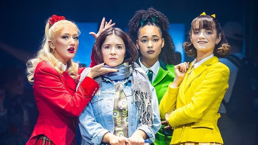 A vibrant theatre stage set for "Heathers," featuring colourful props and dramatic lighting.