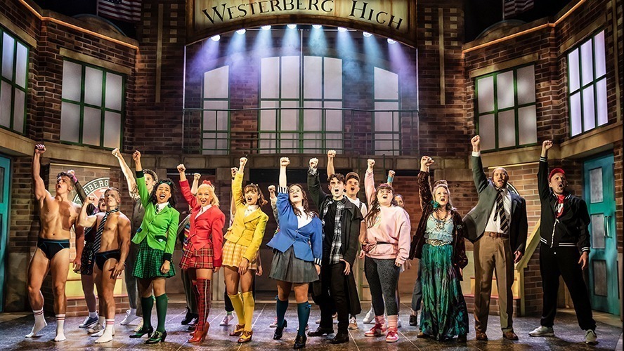 A vibrant theatre stage set for "Heathers," featuring colourful props and dramatic lighting.