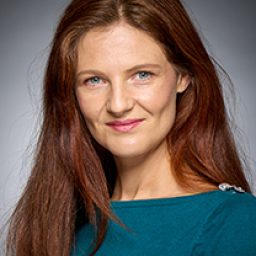 Helen Power in character costume, standing on stage with dramatic lighting and expressive pose.