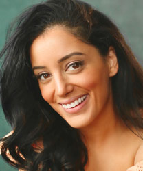 Hiba Elchikhe smiling, wearing a black blazer and white blouse, with long dark hair.