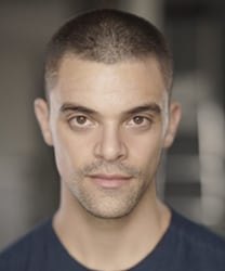 Jacob Fortune-Lloyd smiling, wearing a dark suit and white shirt, with tousled dark hair.