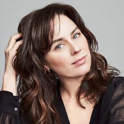 Jill Halfpenny smiling, with shoulder-length dark hair and a black top against a neutral background.