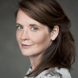 Jo McInnes, smiling, with short brown hair and a black top against a neutral background.