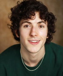 Jordan Broatch smiling, wearing a dark blazer and white shirt, with a blurred background.