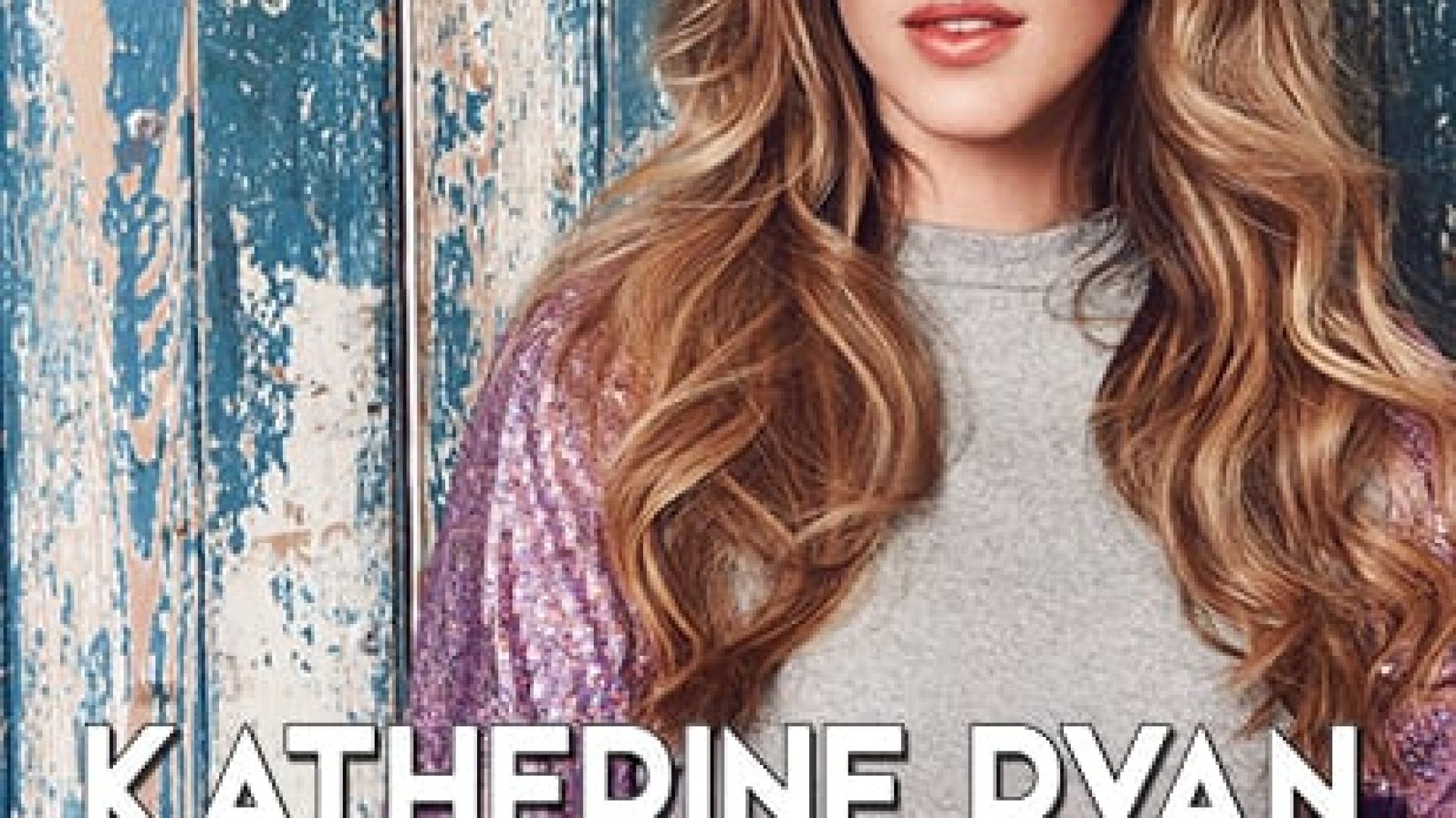 Katherine Ryan smiling, wearing a black top, with long hair styled in loose waves.