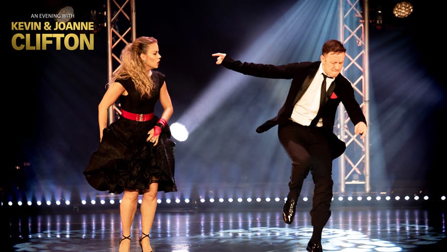 Kevin and Joanne Clifton smiling together, dressed in stylish outfits, against a vibrant backdrop.