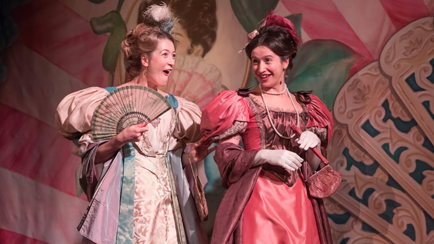 A woman in a Victorian dress holds a fan, surrounded by elegant period decor.