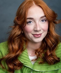 Laura Dawkes smiling, wearing a blue blouse, with shoulder-length brown hair and a neutral background.