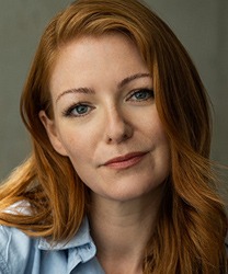 Laura Pitt-Pulford smiling, wearing a black dress, with shoulder-length brown hair and natural makeup.