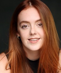 Lauren Byrne smiling, wearing a navy blazer, with shoulder-length brown hair and a neutral background.