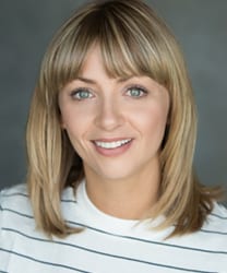 Lisa McGrillis smiling, wearing a blue blouse, with shoulder-length brown hair and a neutral background.