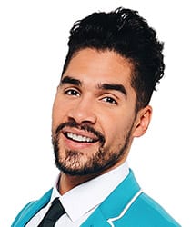 Louis Smith smiling, wearing a dark suit and tie, with a blurred background of an event.