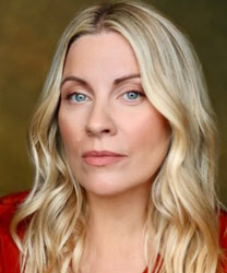 Louise Dearman smiling, wearing a black dress with a silver necklace, against a blurred background.