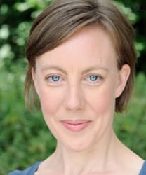 Lucy Tuck smiling, wearing a navy blazer, with shoulder-length brown hair and a neutral background.