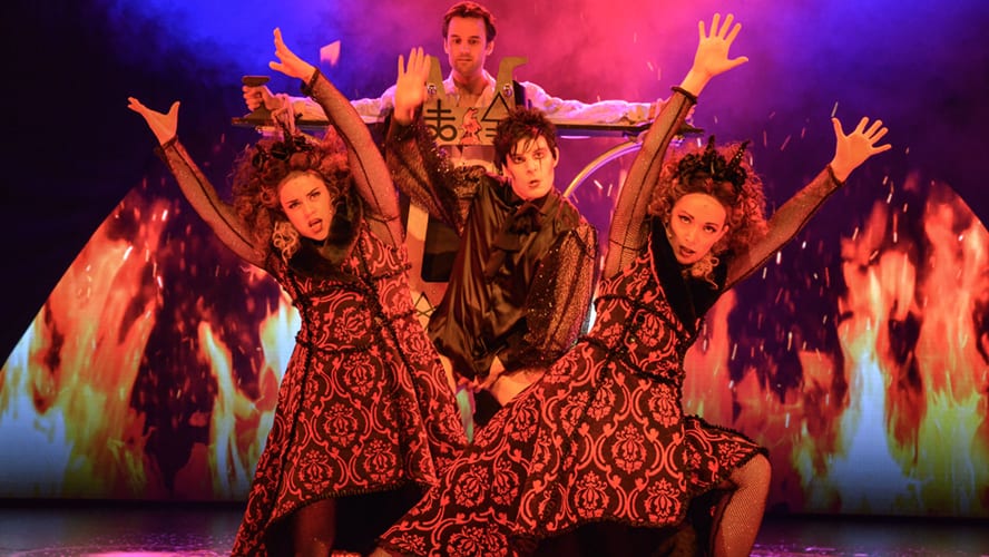 A stage scene featuring actors in vibrant costumes performing a comedic moment with props.