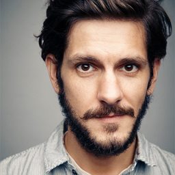 Mat Baynton performing on stage in a theatrical setting, wearing a casual outfit and smiling.
