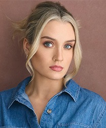 Maddison Firth smiling, wearing a blue blouse, with long brown hair and a neutral background.