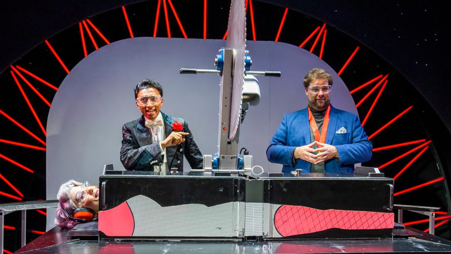 A magician performing on stage at the Apollo Theatre, surrounded by dramatic lighting and props.