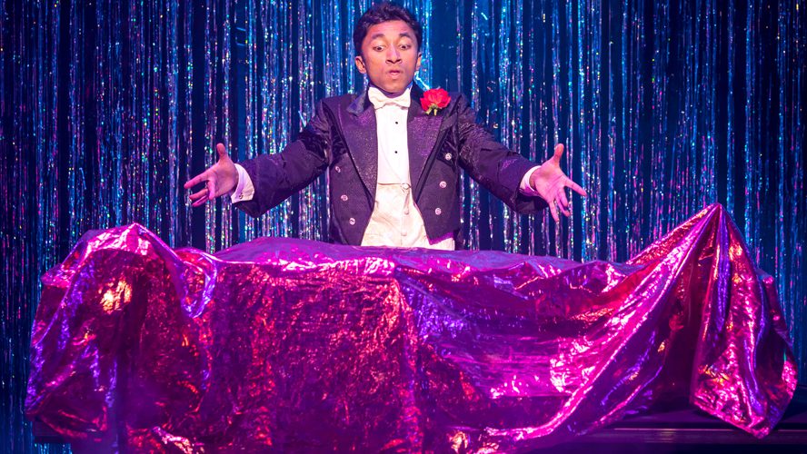 A magician performing on stage at the Apollo Theatre, surrounded by dramatic lighting and props.