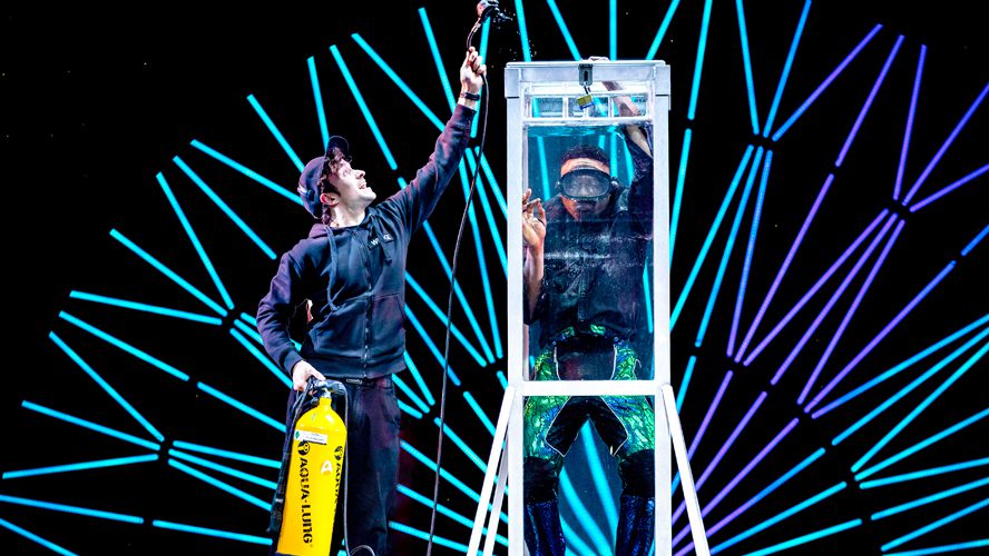 A magician performs on stage at the Apollo Theatre, surrounded by dramatic lighting and props.
