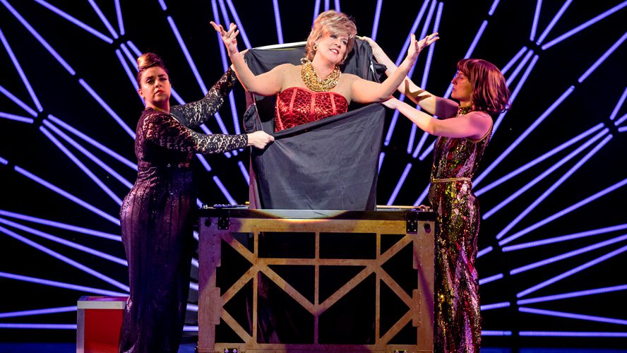 A magician performs on stage at the Apollo Theatre, surrounded by dramatic lighting and props.